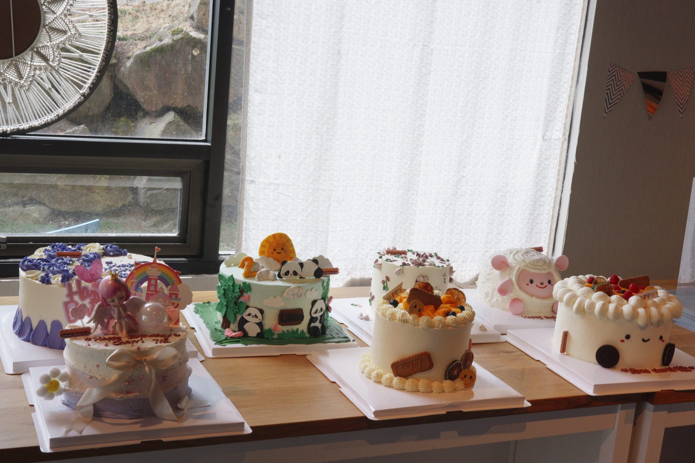 A row of custom character birthday cakes on display at HoneyMe Bakery
